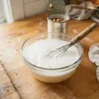 A small bowl of chickpea liquid whisked until foamy, next to an opened can of chickpeas