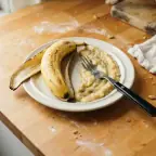 Half a ripe banana mashed with a fork on a small plate