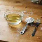 A small bowl of oil and water beside a spoonful of baking powder
