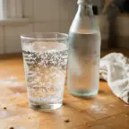 A glass of plain sparkling water full of bubbles, beside an unlabeled bottle